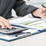 Kobieta podczas prac biurowych wypełniająca formularz oraz licząca na kalkulatorze