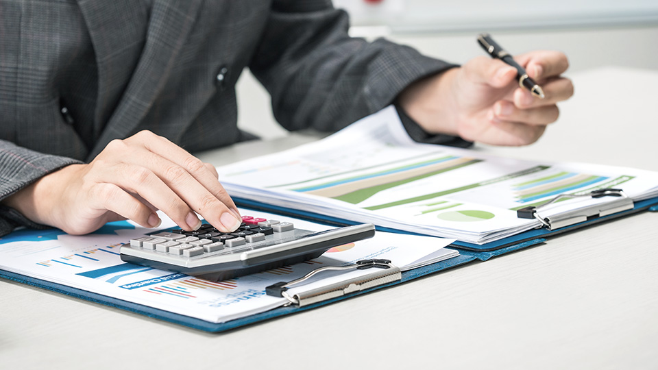 Kobieta podczas prac biurowych wypełniająca formularz oraz licząca na kalkulatorze